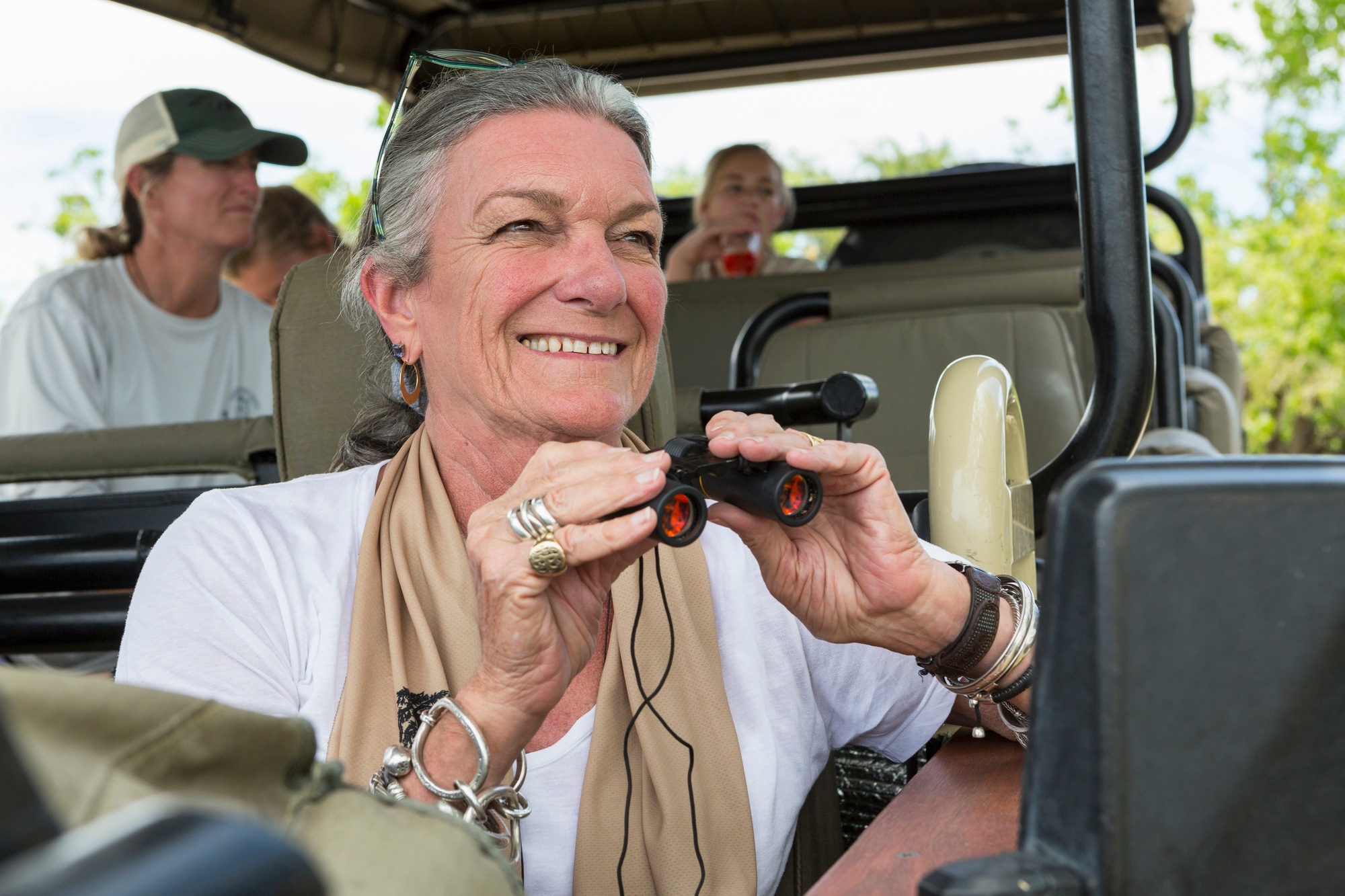 A family in a safari jeep in a wildlife reserve, a seniorwoman with binoculars.