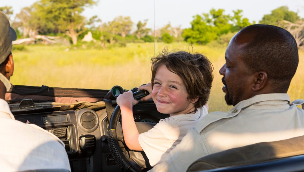 smiling 6 year old boy steering safari vehicle, Botswana