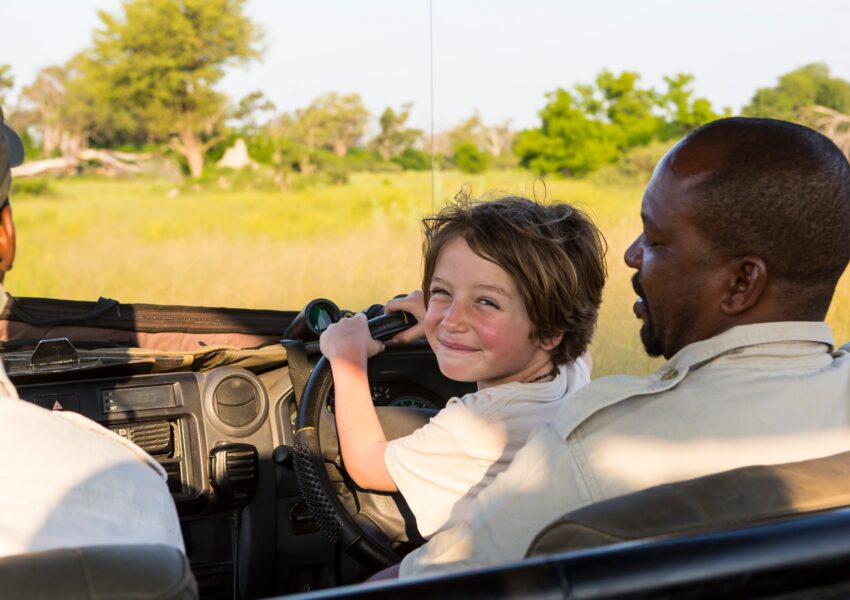 smiling 6 year old boy steering safari vehicle, Botswana