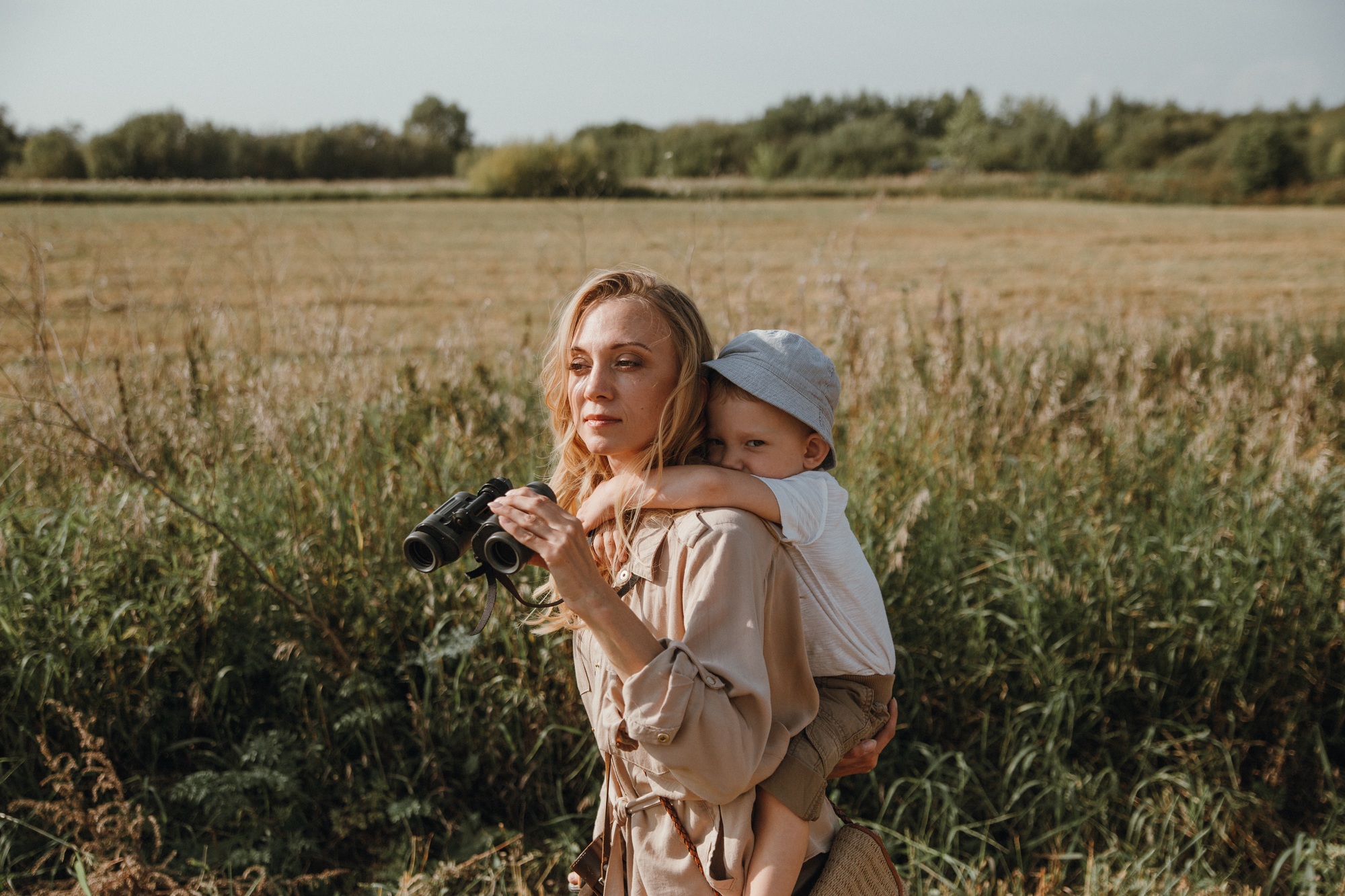 Young woman carries her son on her back and hold binoculars in her hands